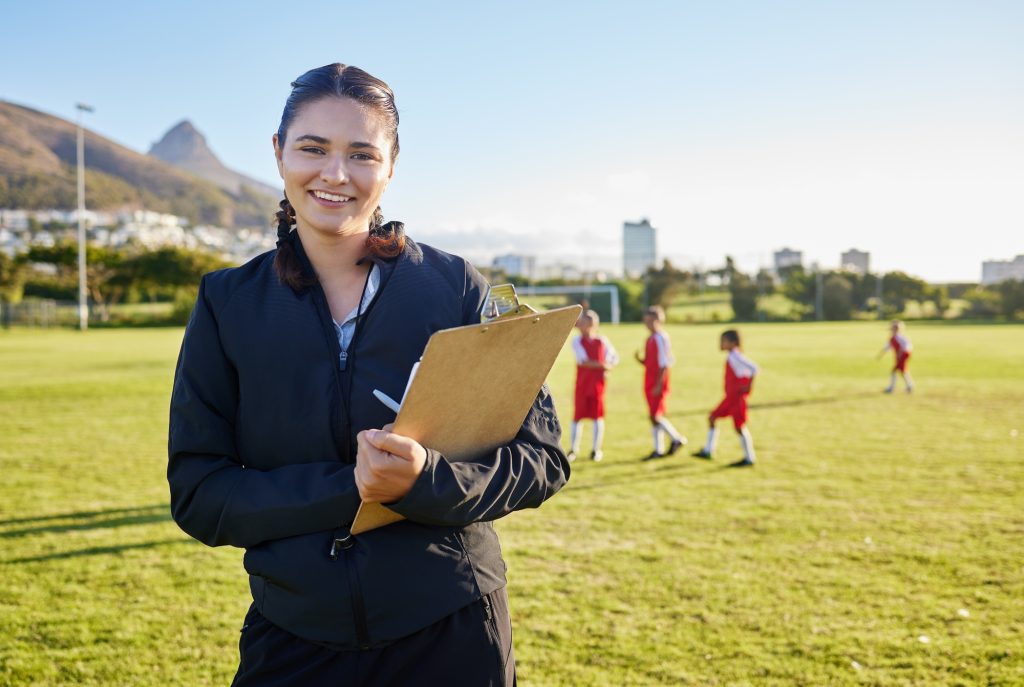 Football coach, junior sports and woman with clipboard coaching children on a soccer field or pitch
