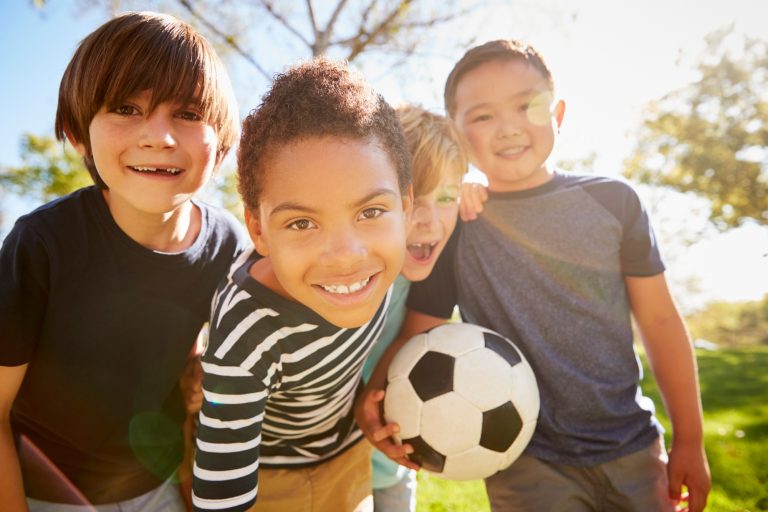 Four young schoolboys leaning in to camera holding football